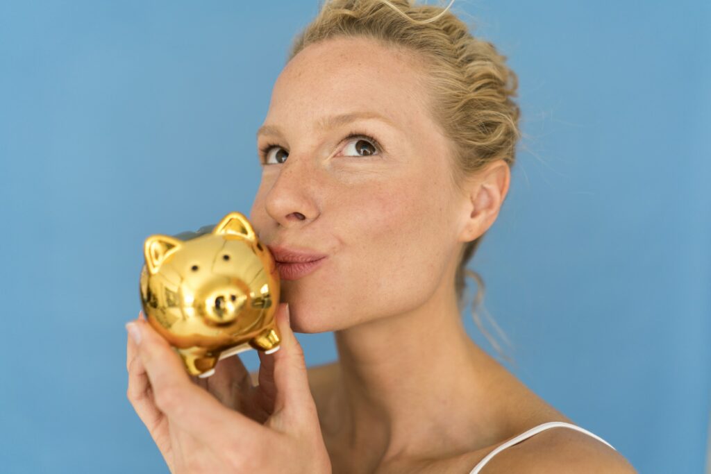 Portrait of blond woman kissing golden piggy bank