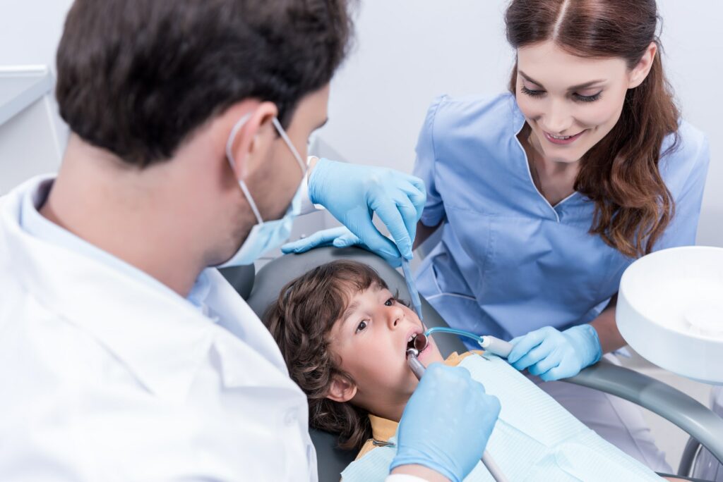 dentists treating teeth of little patient in dentist chair in hospital