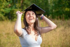 Young woman holding notebook above head like graduate cap and smiling. Insurance online
