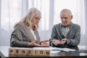 senior couple at table with word 'pension' made of wooden blocks on foreground