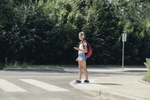 Pretty teenage schoolgirl with headphones and mobile phone on pedestrian crossing