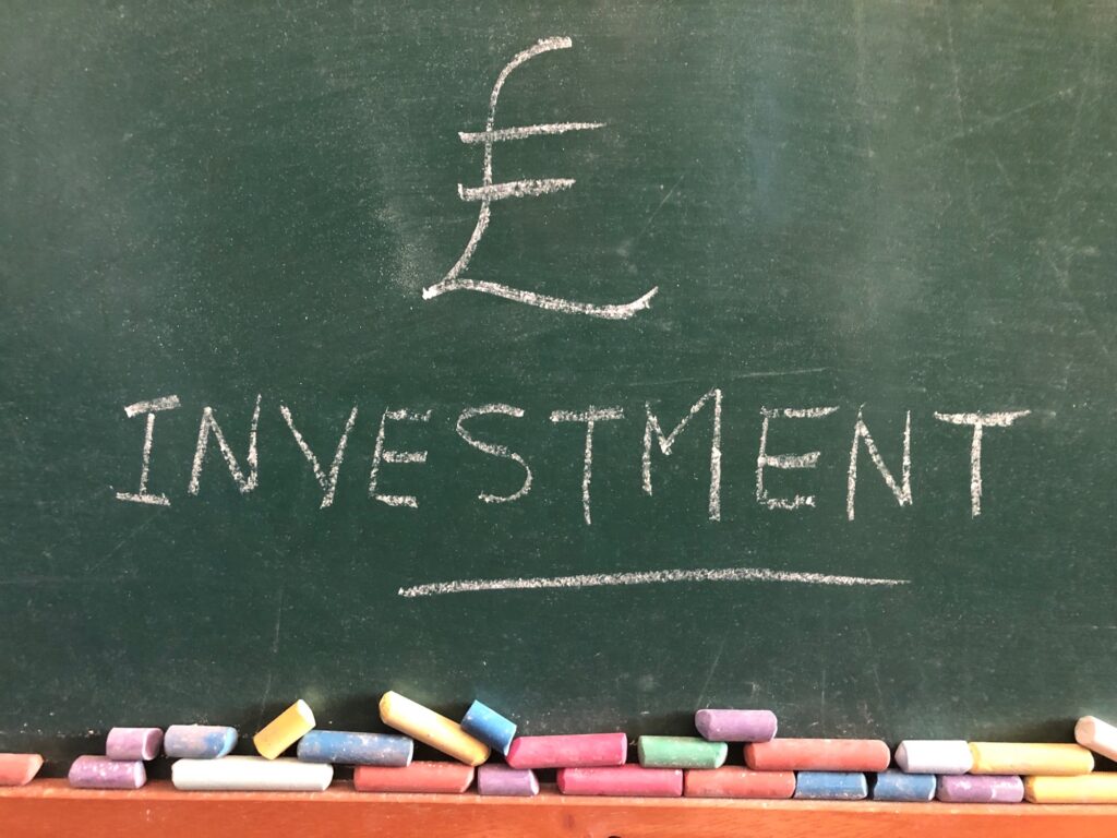 Investment and pound sign on green chalkboard