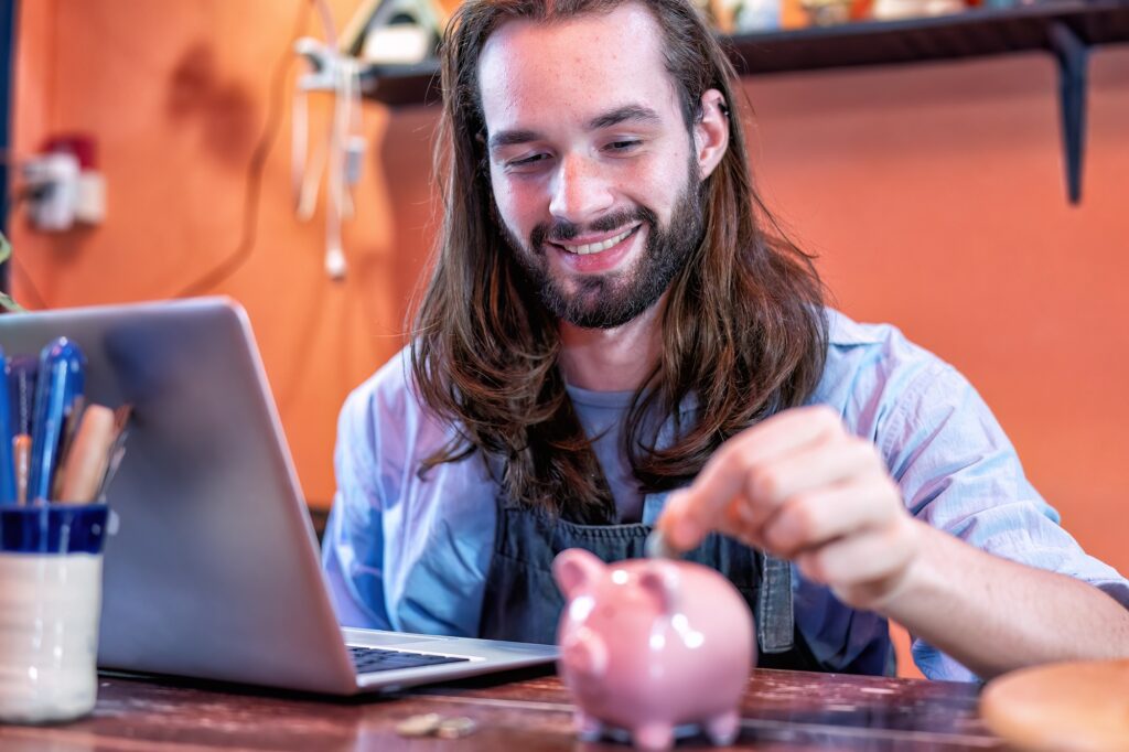 Man working in pottery shop putting coin to piggy bank saving for future pension fund