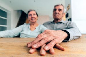elderly couple at home sitting at the table holding hand on hand - focus on hands in foreground